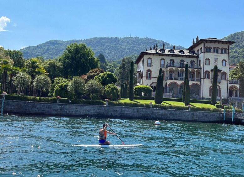 A person paddleboarding on a calm lake with a large, historic building in the background. 3