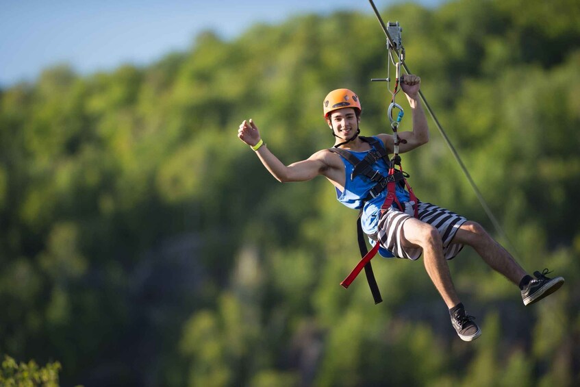 A person engaged in ziplining, wearing a helmet and harness, with a forested landscape in the background. 5