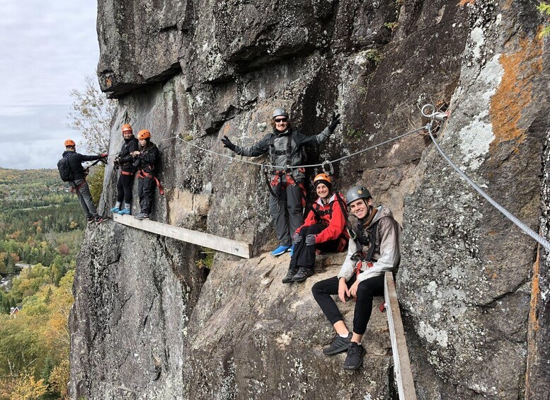 A group of people engaged in a rock climbing activity on a cliff with a rope bridge. 3