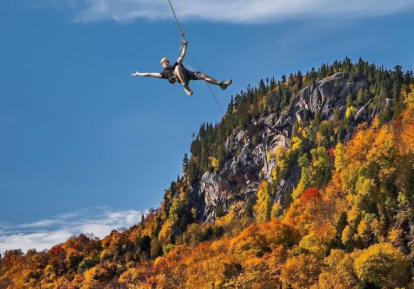 A person bungee jumping from a cliff with autumn foliage. 1