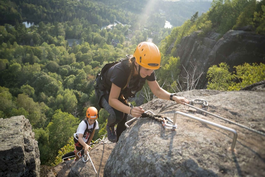 A person in a helmet and harness climbing a rock with a child. 2