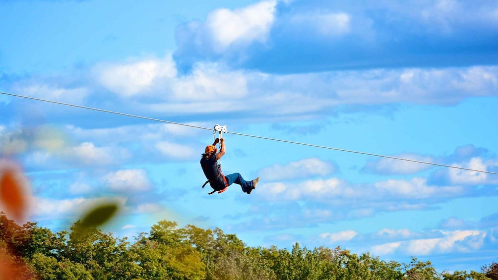 A person ziplining through a clear sky with trees below. 4