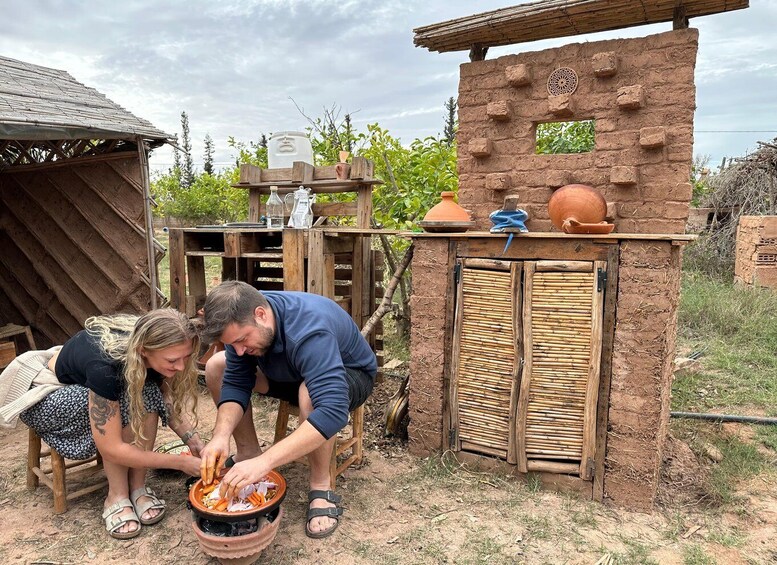 Two people preparing food outdoors with a rustic brick structure and wooden furniture. 1