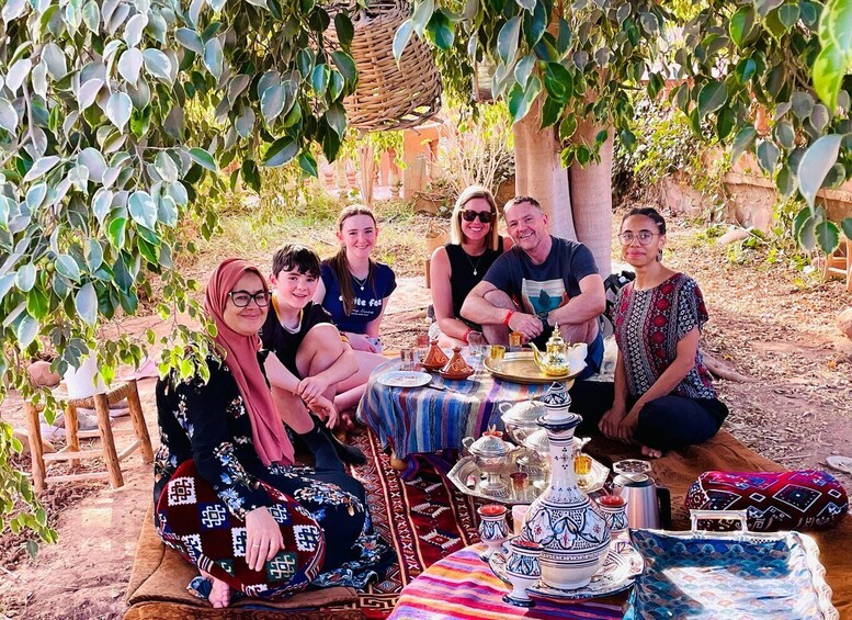 A group of people sitting under a tree with a table set for a meal. 5