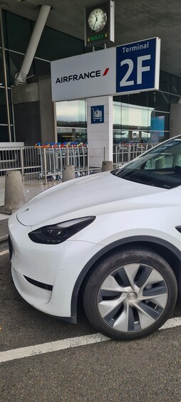 A white car parked near an AirFrance terminal with a clock and a sign indicating Terminal 2F. 2