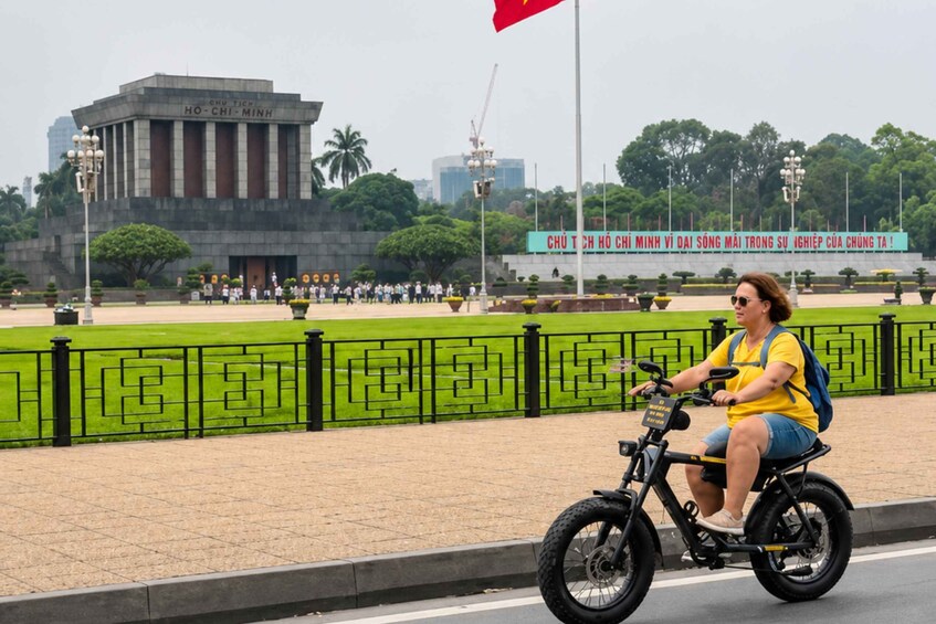 A person riding a black electric scooter on a paved path with a green fence and a monument in the background. 4