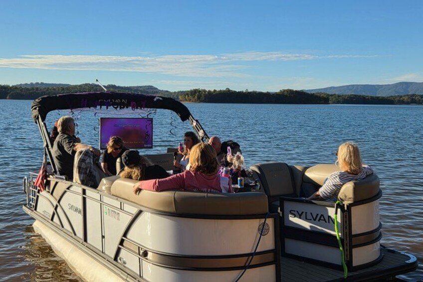 Un bote con gente a bordo, una pantalla mostrando texto y un lago con árboles al fondo. 3