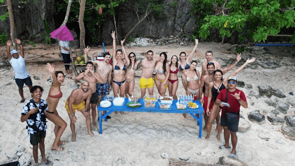 A group of people posing on a sandy beach with a table of food in the center. 5