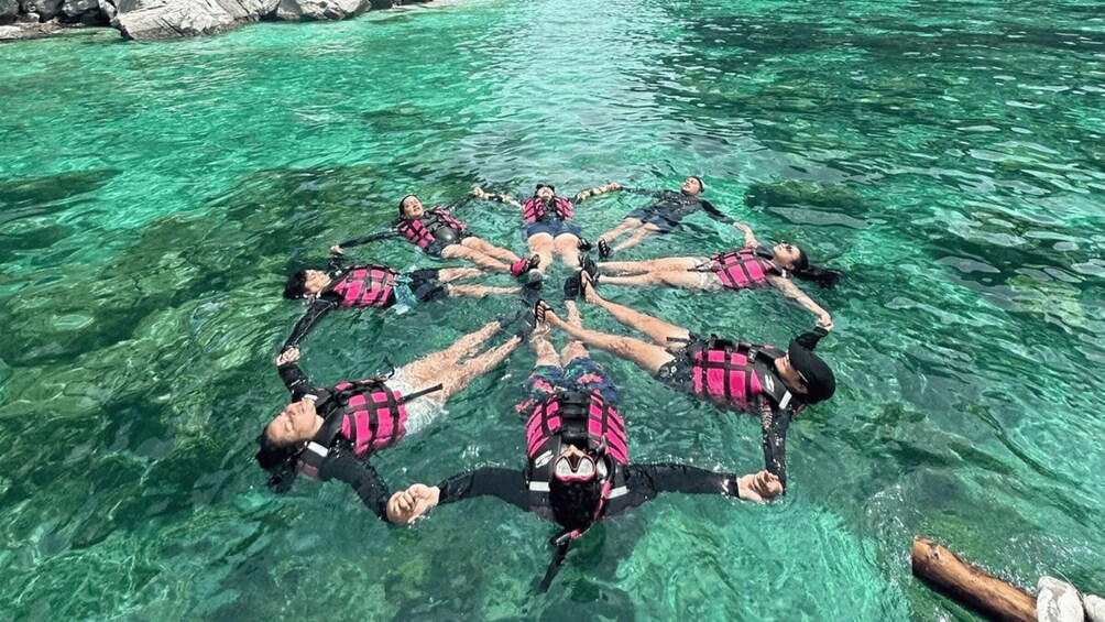 A group of people floating in a circle on a clear body of water. 1