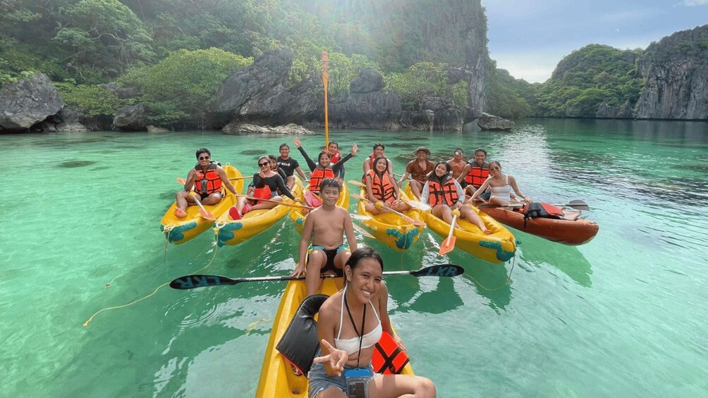A group of people in colorful kayaks on a calm, turquoise body of water surrounded by lush greenery and rocky cliffs. 3