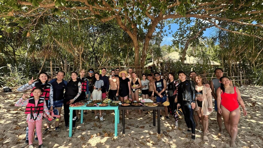 A group of people gathered around a table on a sandy beach with trees in the background. 4