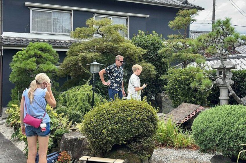 A residential area with a traditional Japanese-style garden, including a stone lantern, neatly trimmed bushes, and a small pond. 2