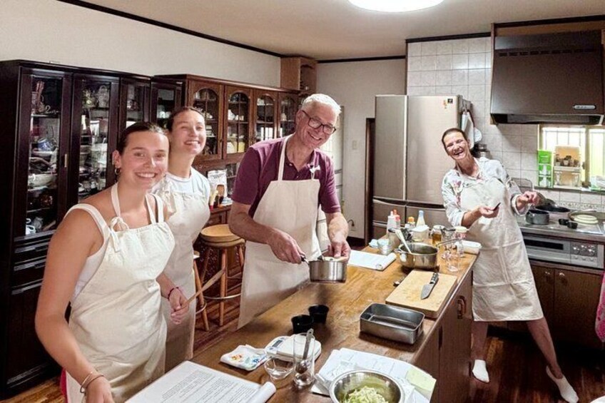 A kitchen with four people wearing aprons, a wooden table with cooking utensils, and a refrigerator. 1