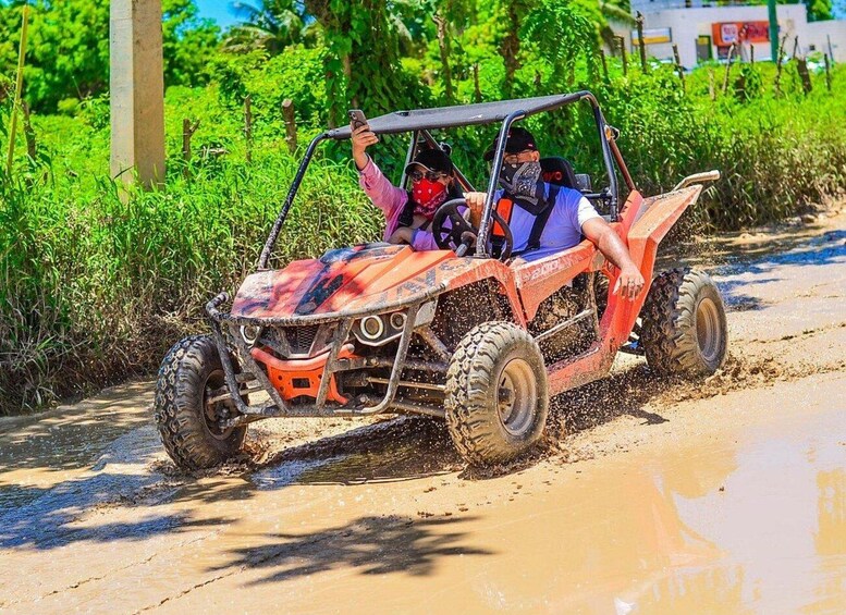 A red off-road vehicle driving through a muddy path with vegetation on the sides. 5
