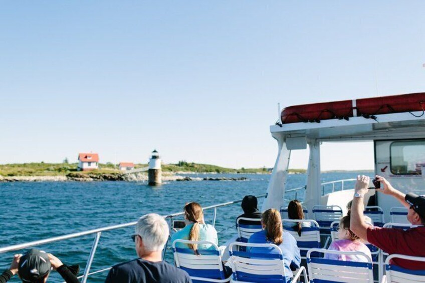 A boat with passengers looking at a lighthouse. 1