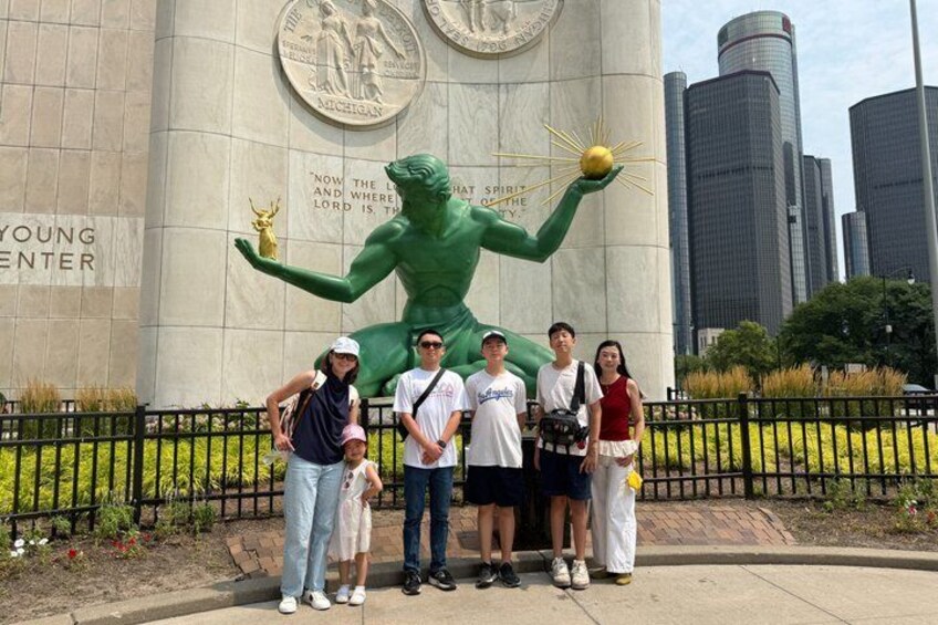 A group of people standing in front of a large green statue with a golden ball, with a city skyline in the background. 4