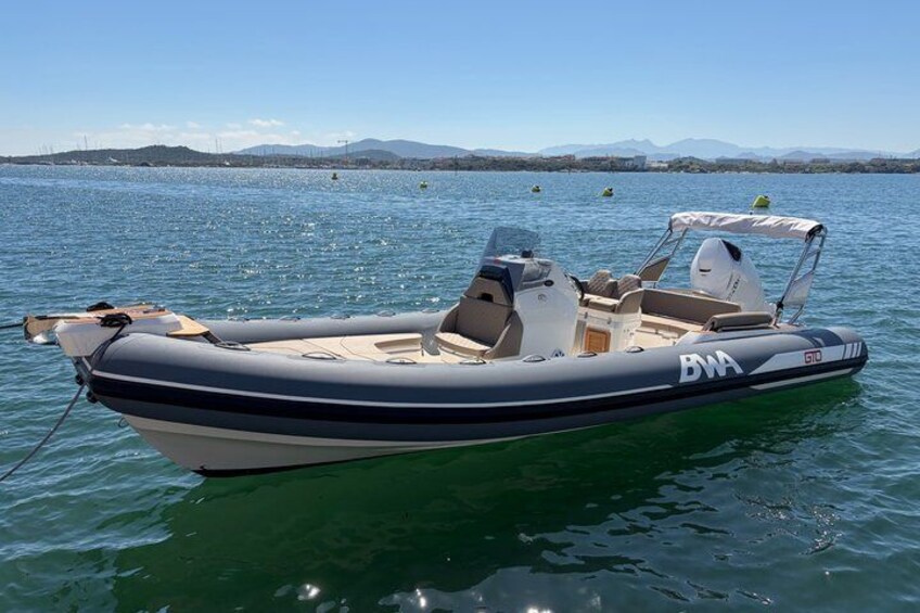 A motorboat with the logo 'BNA' on its side, floating on calm water with a clear sky and distant mountains in the background. 2