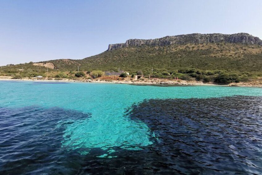 A coastal landscape with clear turquoise waters, a sandy beach, and a rocky hill with sparse vegetation. 4