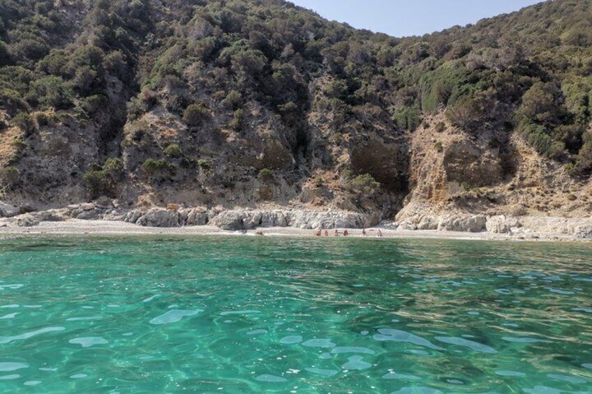A coastal landscape with clear turquoise water, rocky cliffs, and sparse vegetation. 3