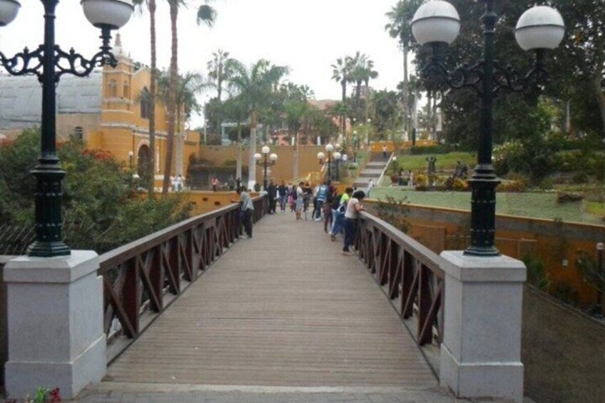 A wooden bridge with railings, surrounded by greenery and palm trees. 5