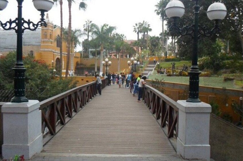 A wooden bridge with railings, surrounded by greenery and palm trees. 5