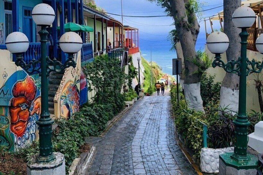 A cobblestone street with colorful buildings, a mural, and street lamps. 3