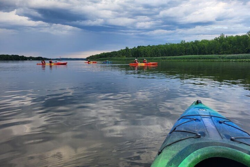 A calm lake with kayaks and a green kayak in the foreground. 1