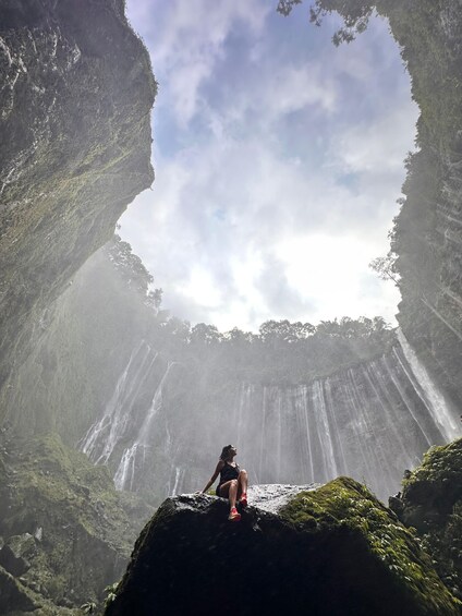 A person sitting on a rock with a waterfall in the background. 2