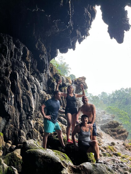A group of people standing on rocky terrain with a cave opening behind them. 5