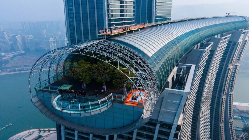 A modern architectural structure with a curved glass facade, a rooftop garden, and a bridge extending from the building. 1