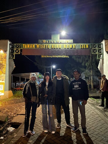 A group of people standing in front of a sign with text in a foreign language. 1