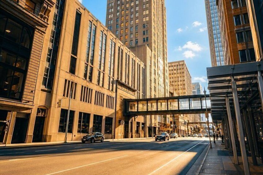 A city street with tall buildings, a pedestrian overpass, and cars on the road. 4
