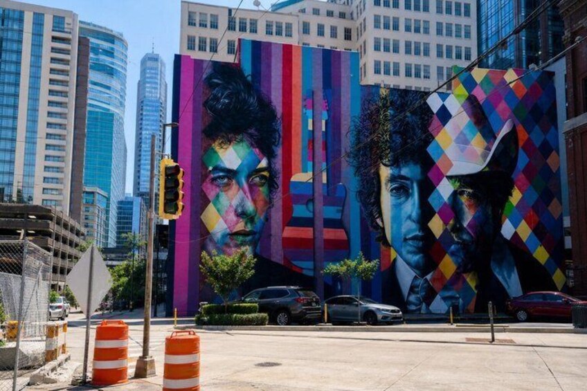 A city street with a large colorful mural on a building, traffic cones, and a traffic light. 5