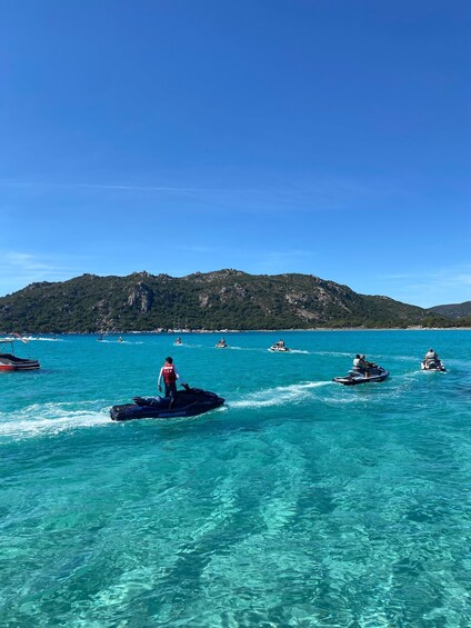 Clear turquoise water, jet skis, and a mountainous landscape in the background. 1