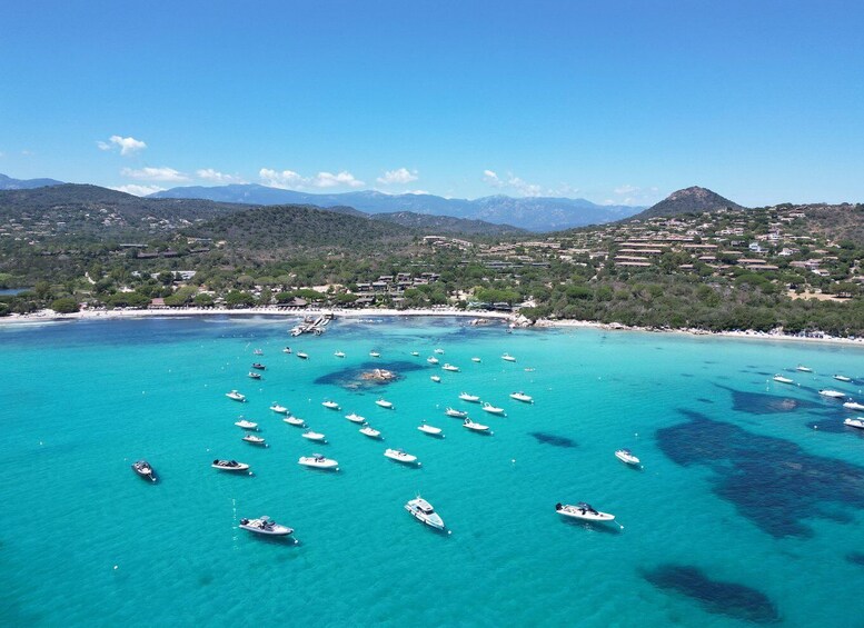A coastal town with boats on turquoise waters, surrounded by mountains and greenery. 2