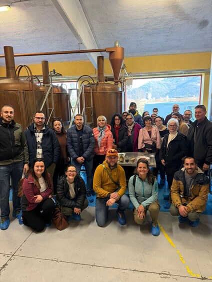 A group of people in a brewery setting with large copper brewing equipment. 3