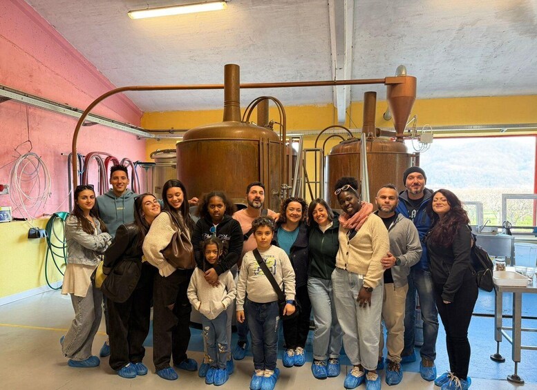 A group of people in a brewery with large copper fermenters and a pink wall. 5