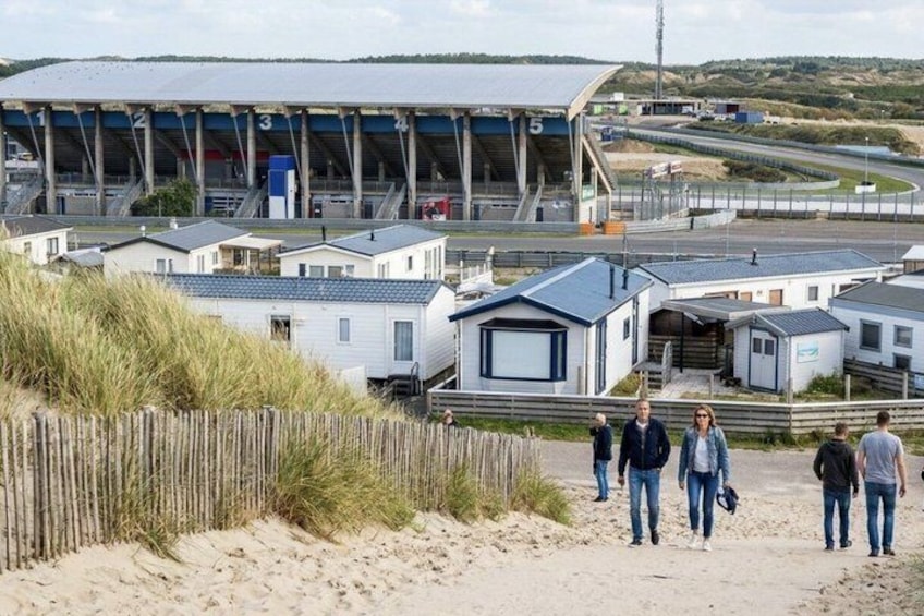 A beachside caravan park with mobile homes, a sandy path, and a large sports stadium in the background. 2