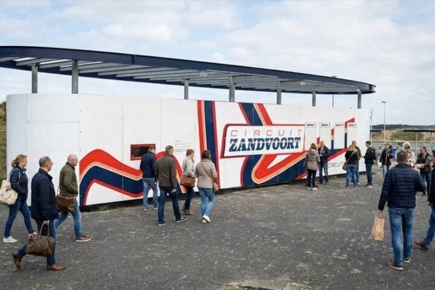 A group of people walking towards a building with a large sign reading 'CIRCUIT ZANDVOORT'. 1