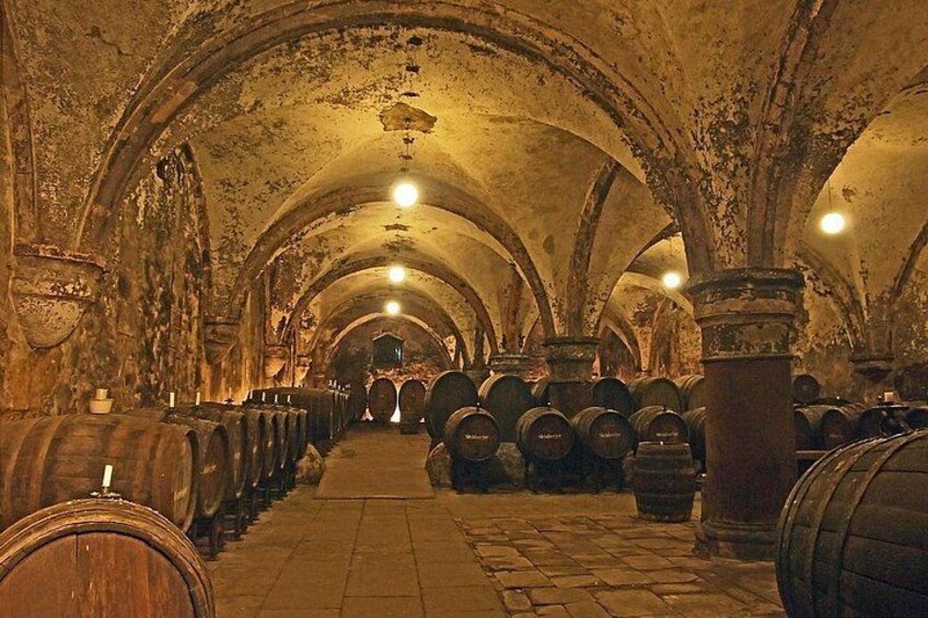 A dimly lit underground wine cellar with rows of wooden barrels and arched ceilings. 2