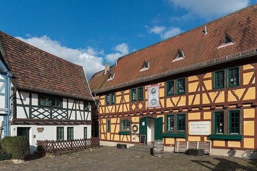 A traditional half-timbered building with a green door and windows, a cobblestone courtyard, and a clear blue sky. 5