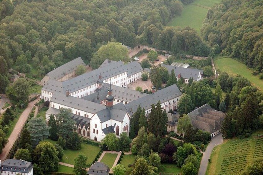 A large, historic building complex surrounded by lush greenery and a well-maintained garden. 1
