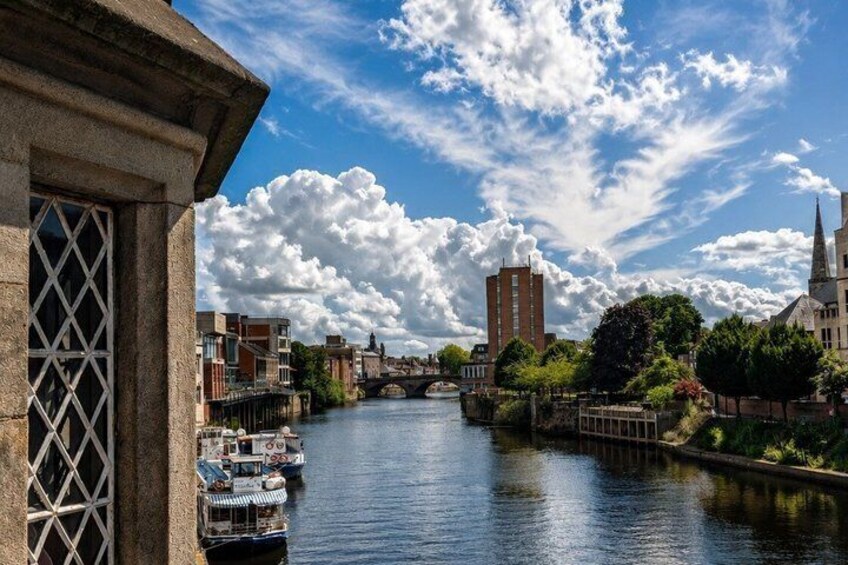 A river with boats, a bridge, and buildings under a partly cloudy sky. 3