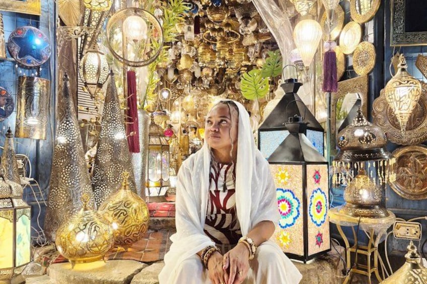 A person sitting in a shop filled with ornate lamps and decorative items. 1