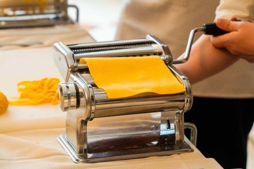 A person using a pasta machine to roll out dough. 2