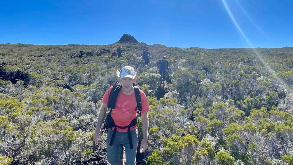 Un randonneur, vêtu d’un t-shirt et d’une casquette rouges, traverse un paysage aride et couvert de broussailles, avec une montagne en arrière-plan. 3