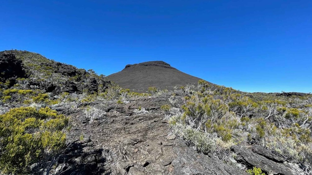 Un paysage volcanique caractérisé par une montagne imposante, une végétation clairsemée et un ciel bleu dégagé. 1