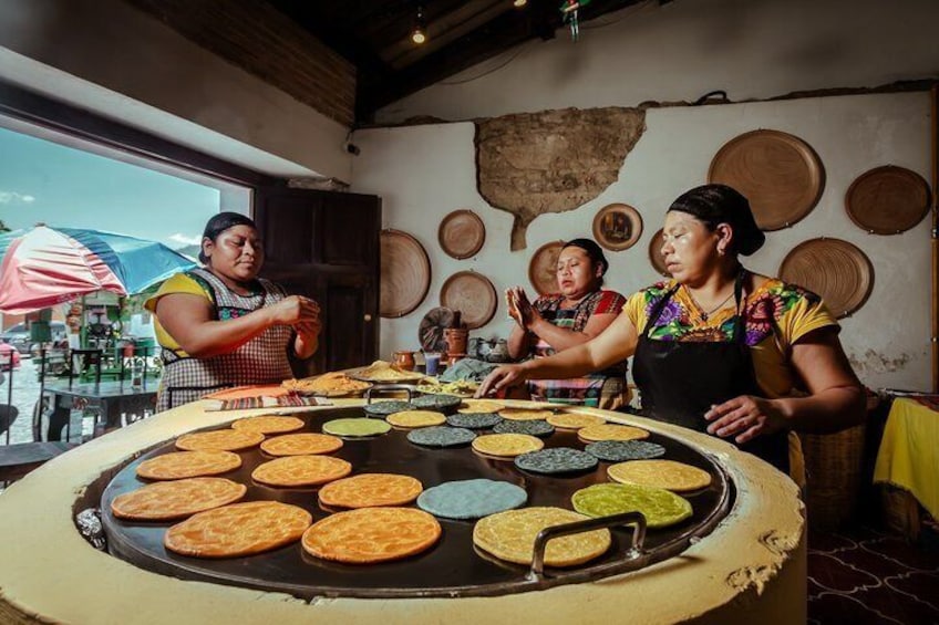 A cooking area with a large griddle, people cooking, and traditional round mats on the wall. 1