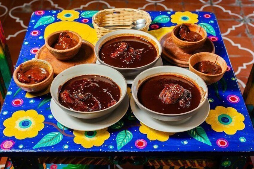 A table with bowls of red sauce, possibly a stew, on a colorful tablecloth with floral patterns. 2