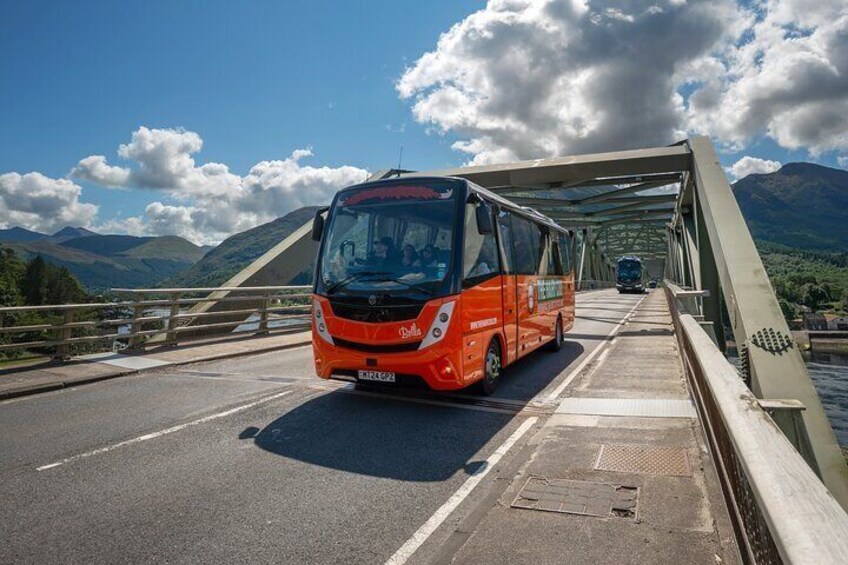 A red bus on a bridge with mountains in the background. 3